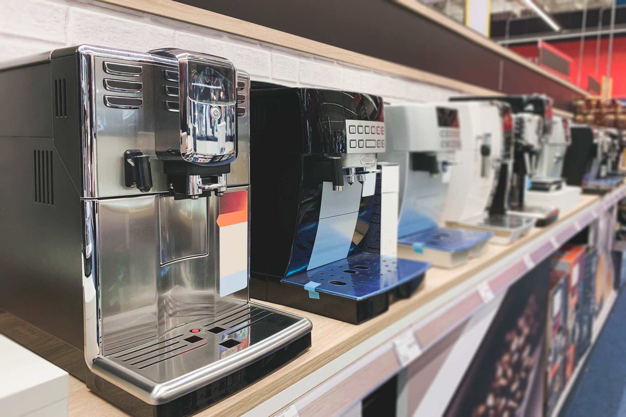 Macchine da caffè superautomatiche in acciaio, nere e bianche, in fila su uno scaffale in legno chiaro di un negozio